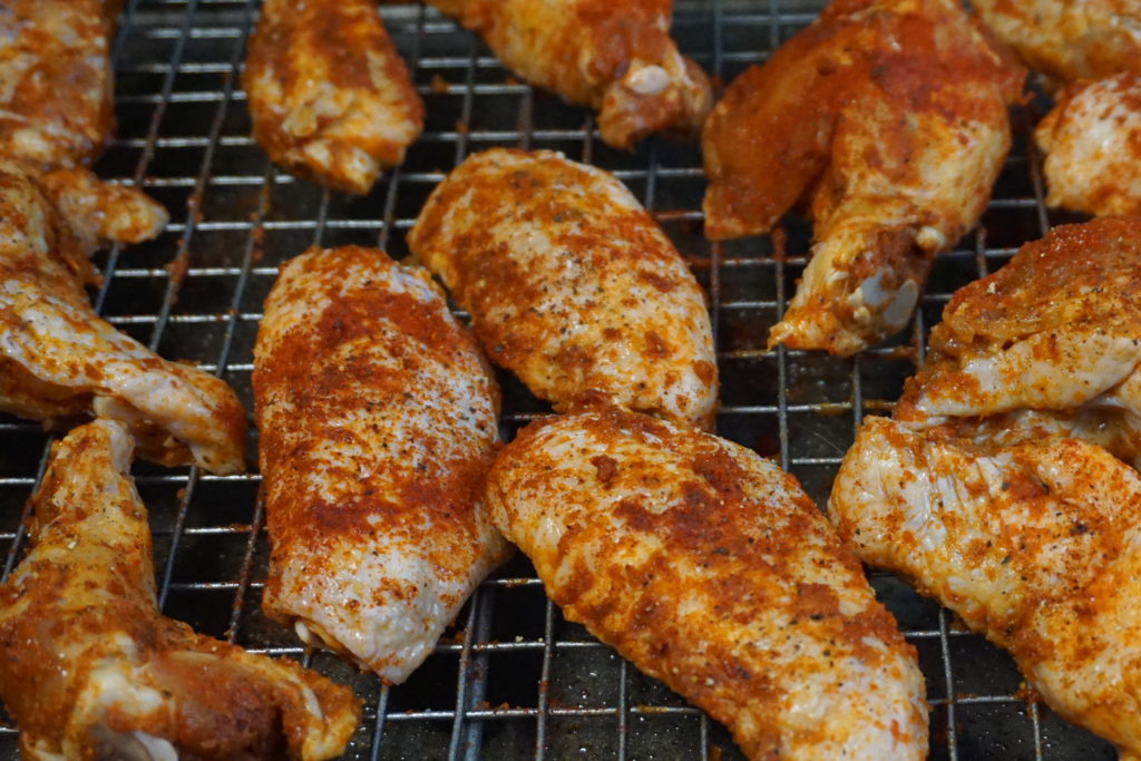 Uncooked chicken wings on a rack with the dry rub. 