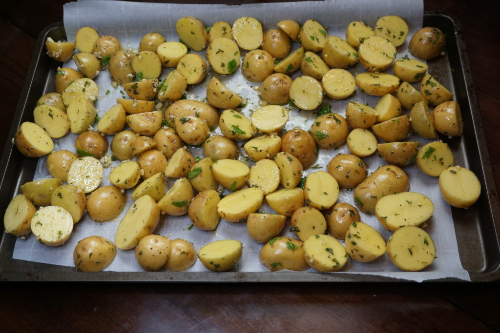 Before roasting. Garlic potatoes spread out on a lined parchment paper cookie sheet. 