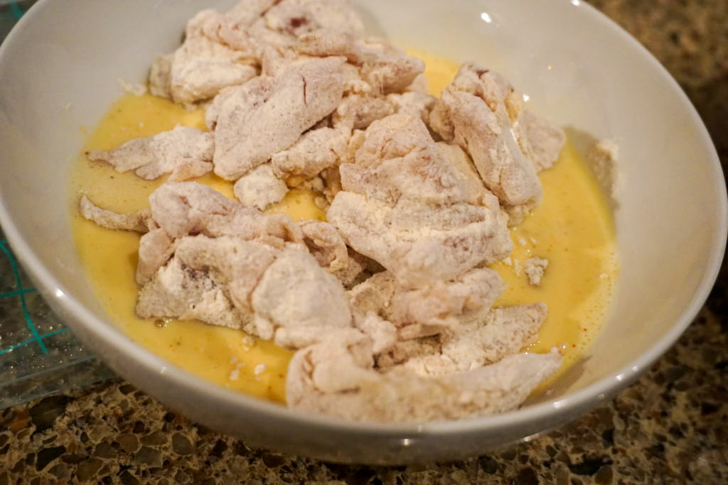 Flour chicken thighs going into the egg wash with buttermilk