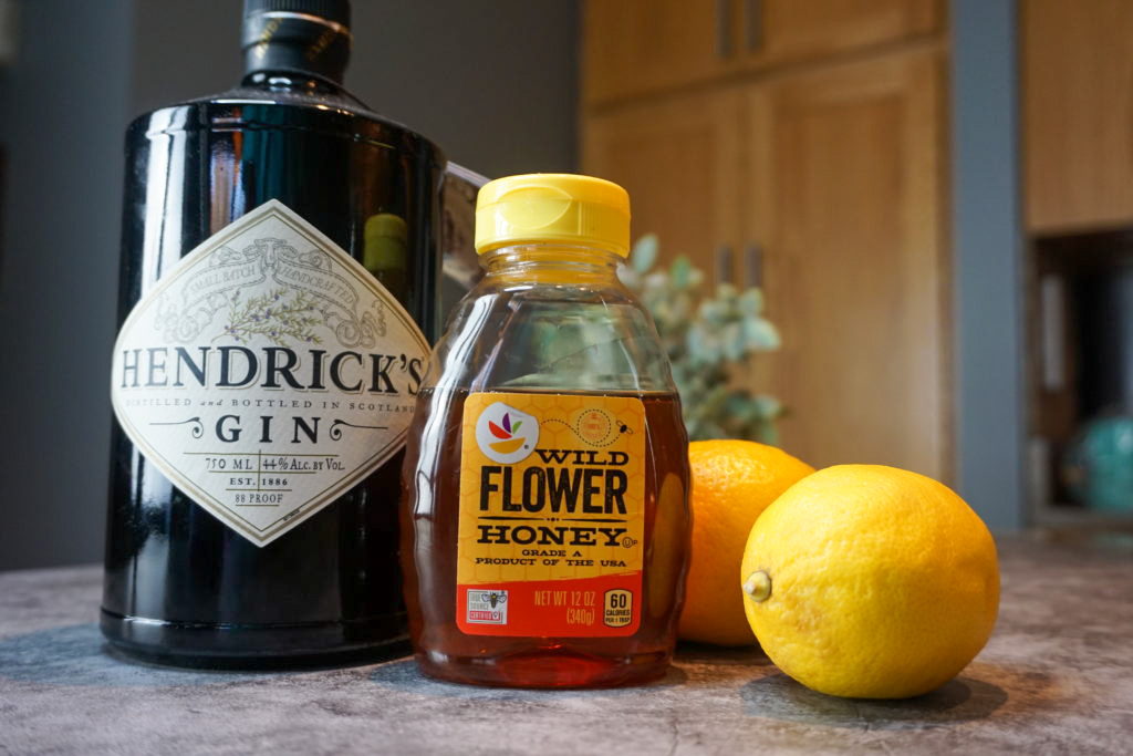 the ingredients for the bee's knees cocktail: gin, honey, and fresh lemons