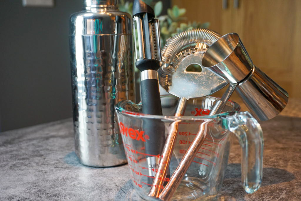 The tools used to the make the cocktail: cocktail shaker, peeler, strainer, jigger, and measuring cup