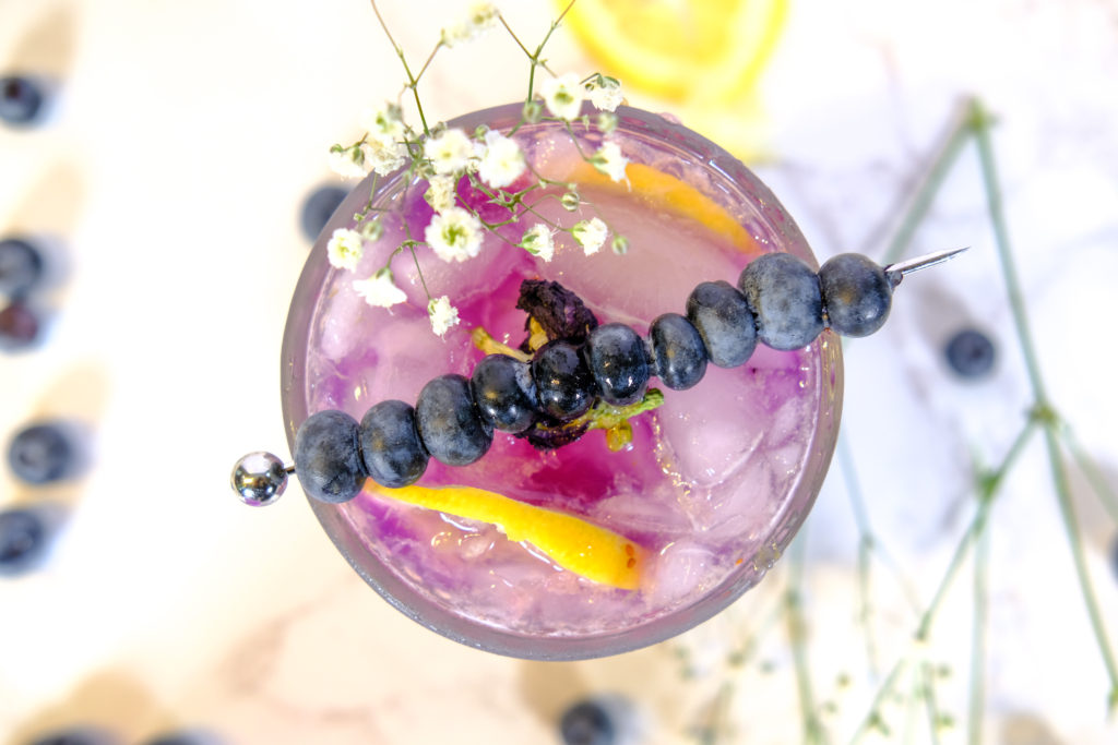 overlook of the purple delight cocktail with blueberries, flowers, and lemon slices