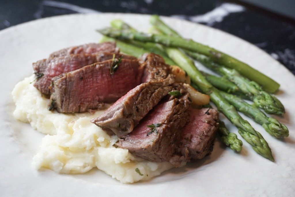 Filet mignon served with mashed potatoes, herbs, and asparagus. 