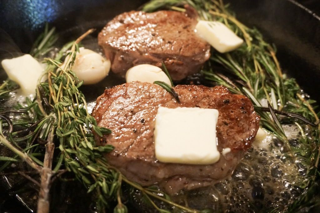 Pan frying the steak with garlic, fresh herbs, and unsalted butter