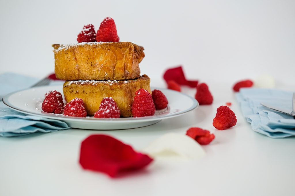 wide angle of the pain perdu plated with powdered sugar, raspberries, and rose petals