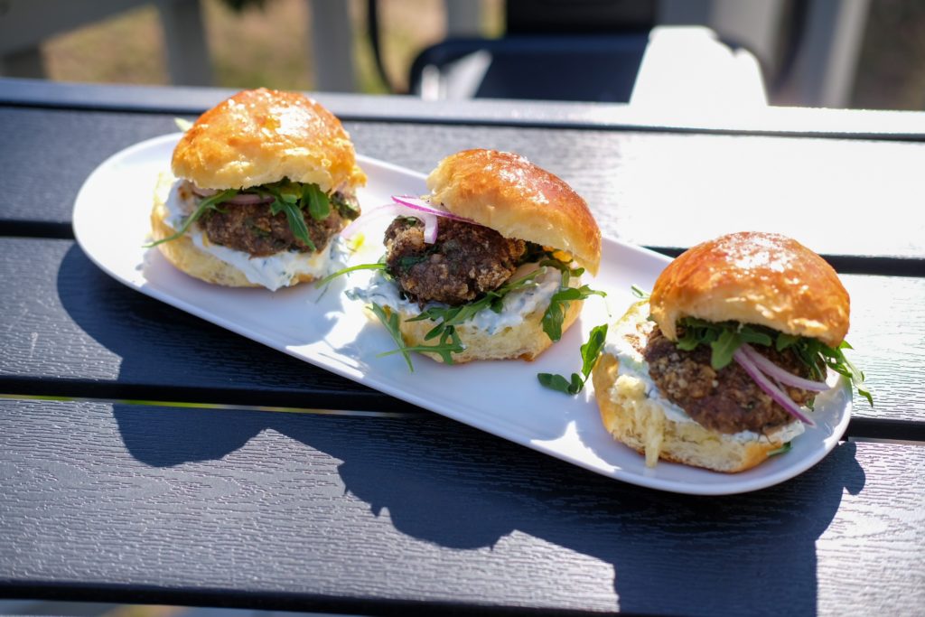 the beef walnut sliders plated with onions, arugula, and tzatziki sauce 