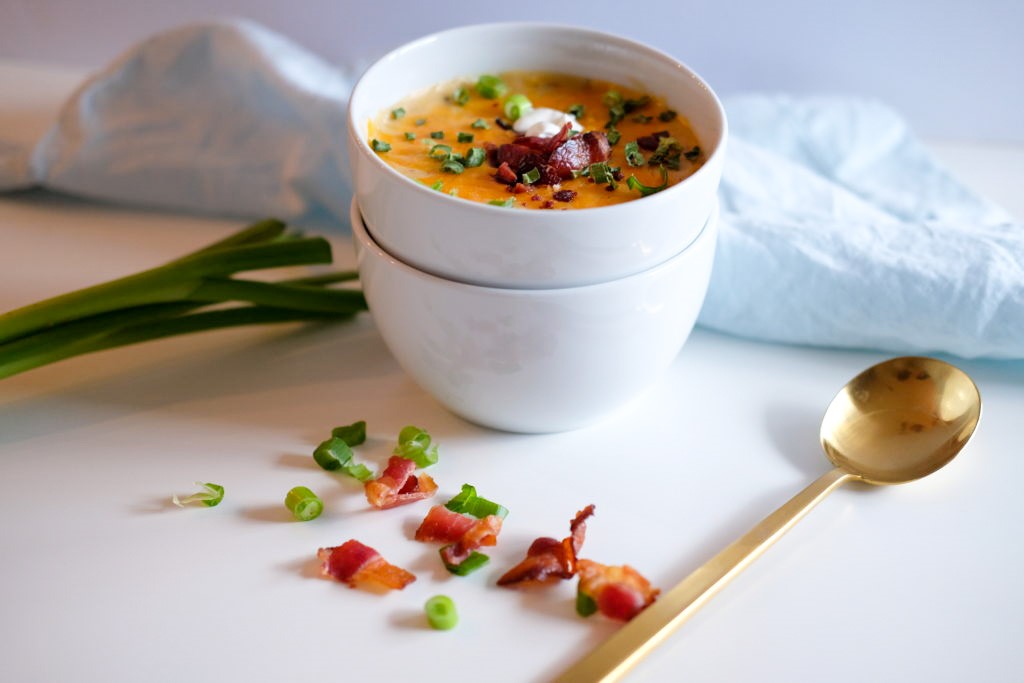 two bowls, one containing the loaded potato soup with a spoon, bacon, and green onion